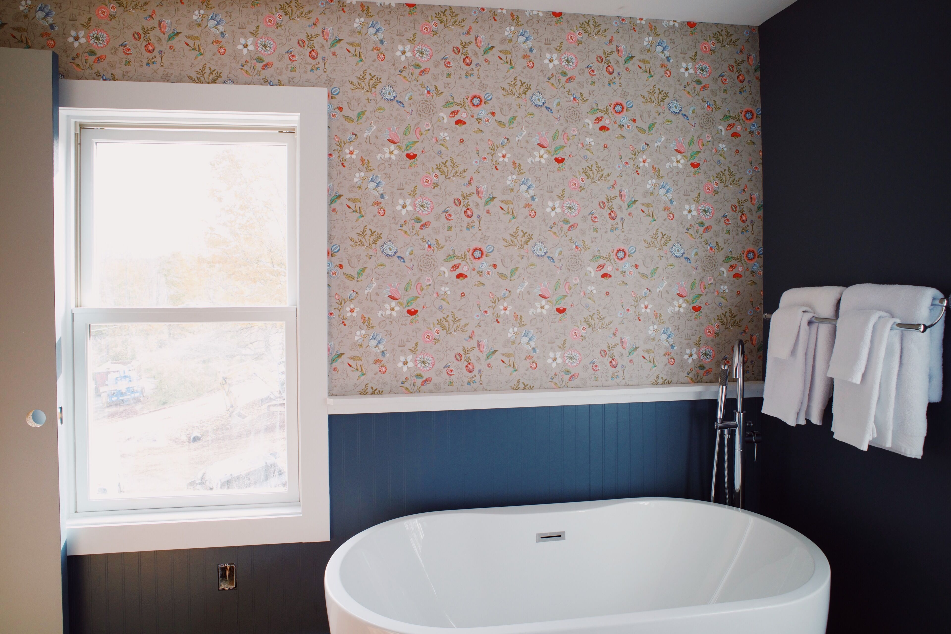 Un baño con una bañera independiente, una ventana y una pared con papel tapiz floral.