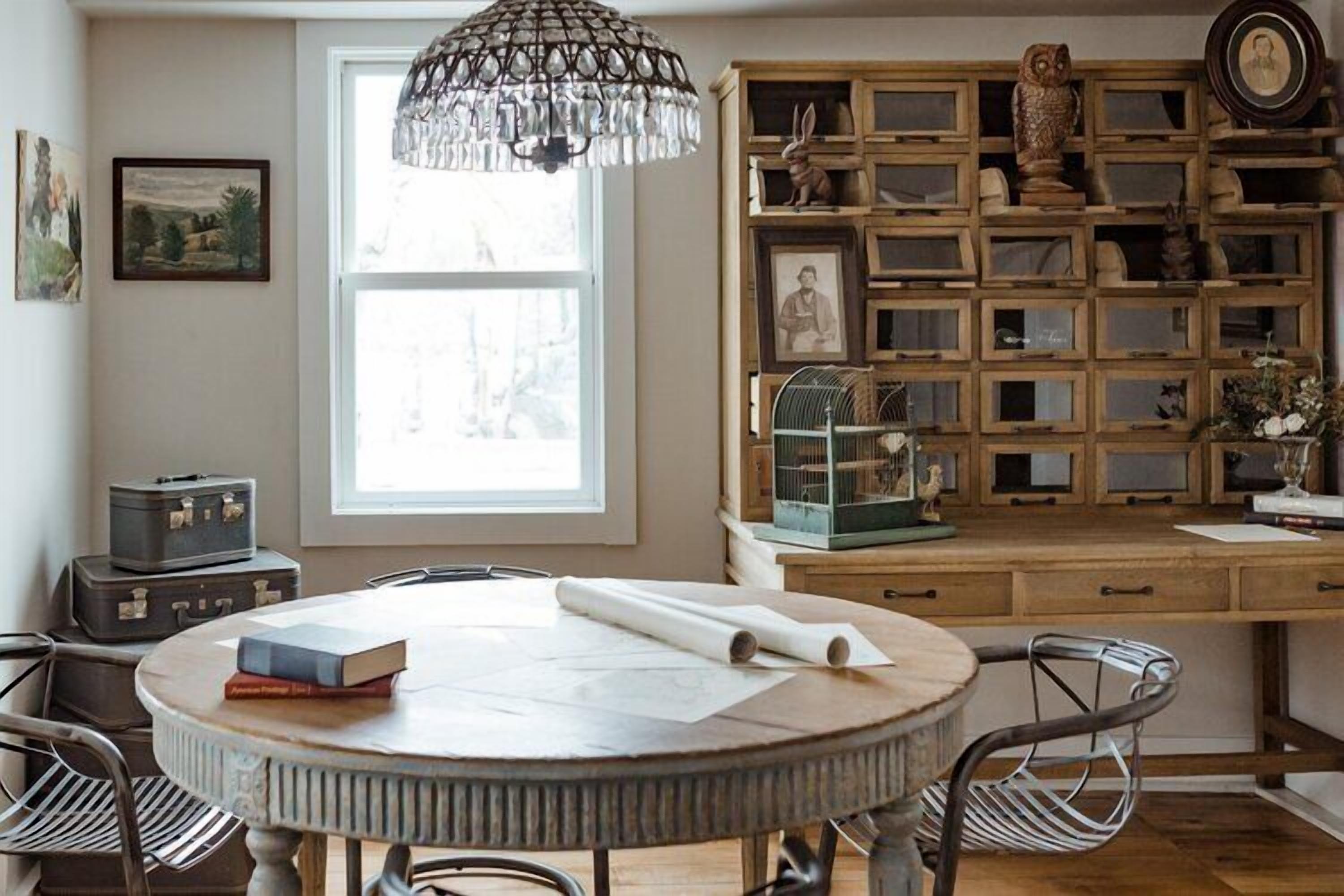 A room with a round wooden table, chairs, a window, and a wall of wooden display cases with various items.