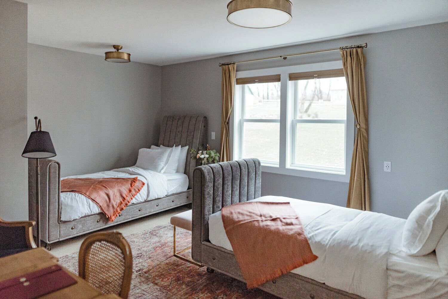 A bedroom with two beds, a desk, a chair, a lamp, and a window with curtains.