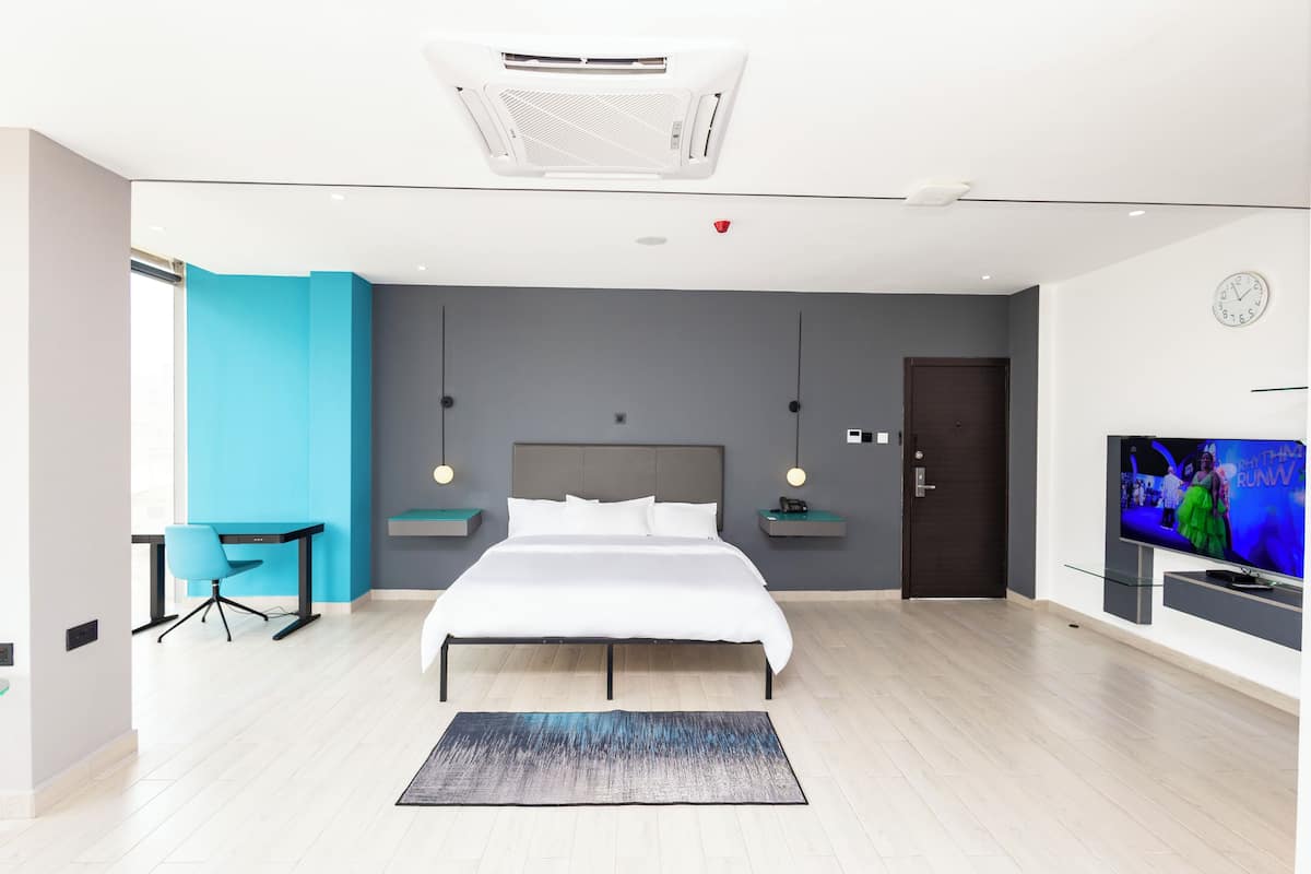A modern bedroom with a bed, a desk, a chair, a TV, and a clock on the wall.