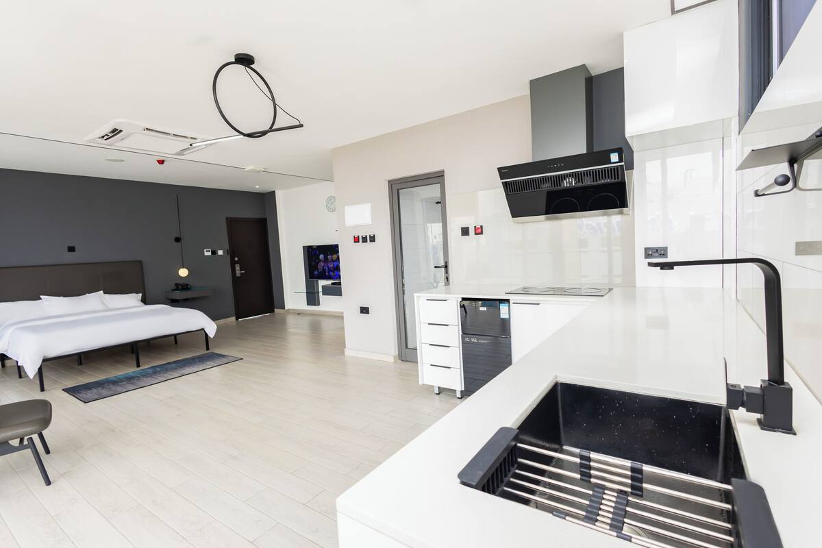 A modern hotel room with a bed, a desk, a kitchenette, and a bathroom.