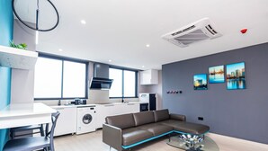 A modern kitchen with a built-in oven, a dining area with a white table and chairs, a brown sofa, and a glass coffee table. - Bankable Roomzzz (Accra)