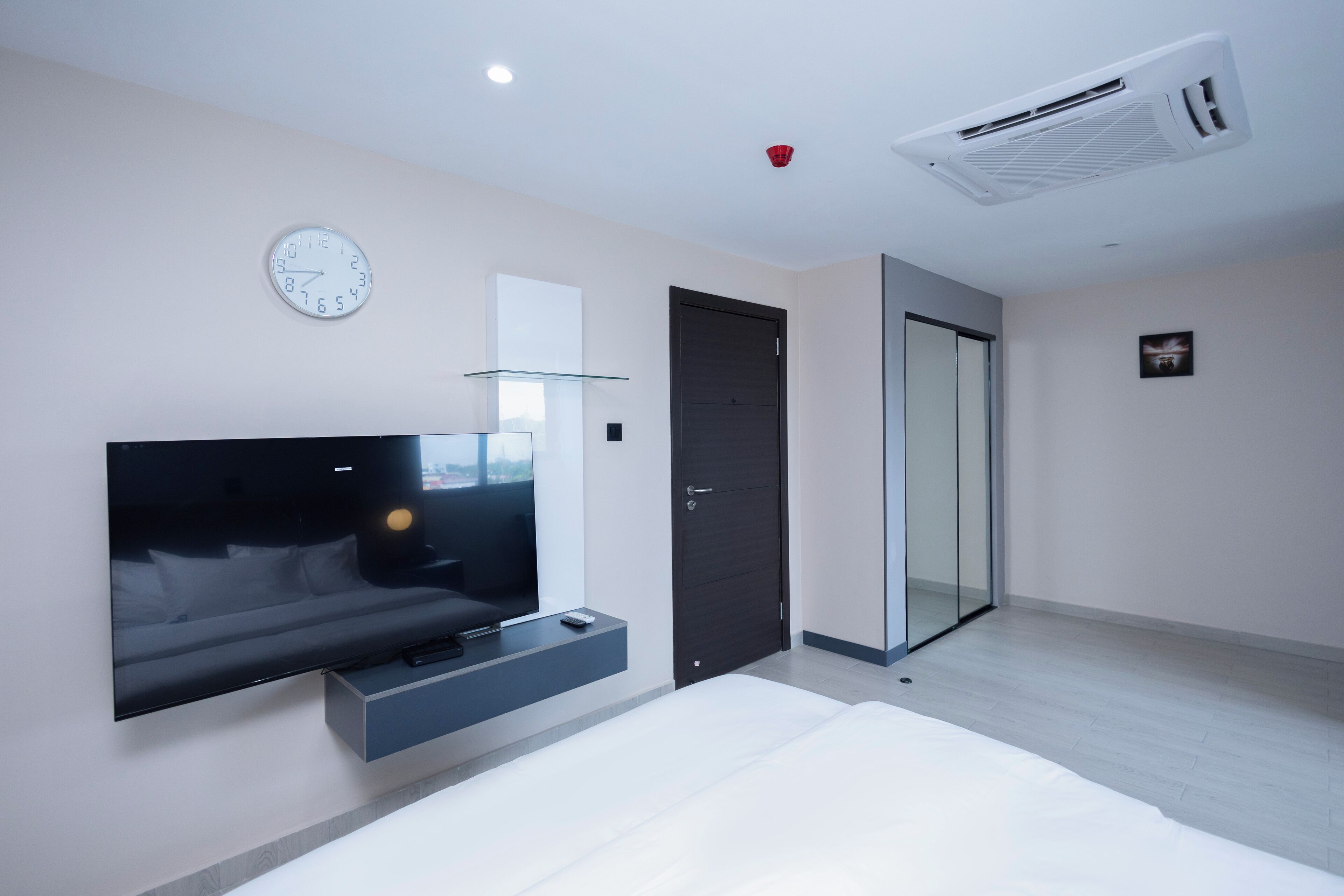 A modern bedroom with a large bed, a mounted TV, a glass door, and a wall clock.