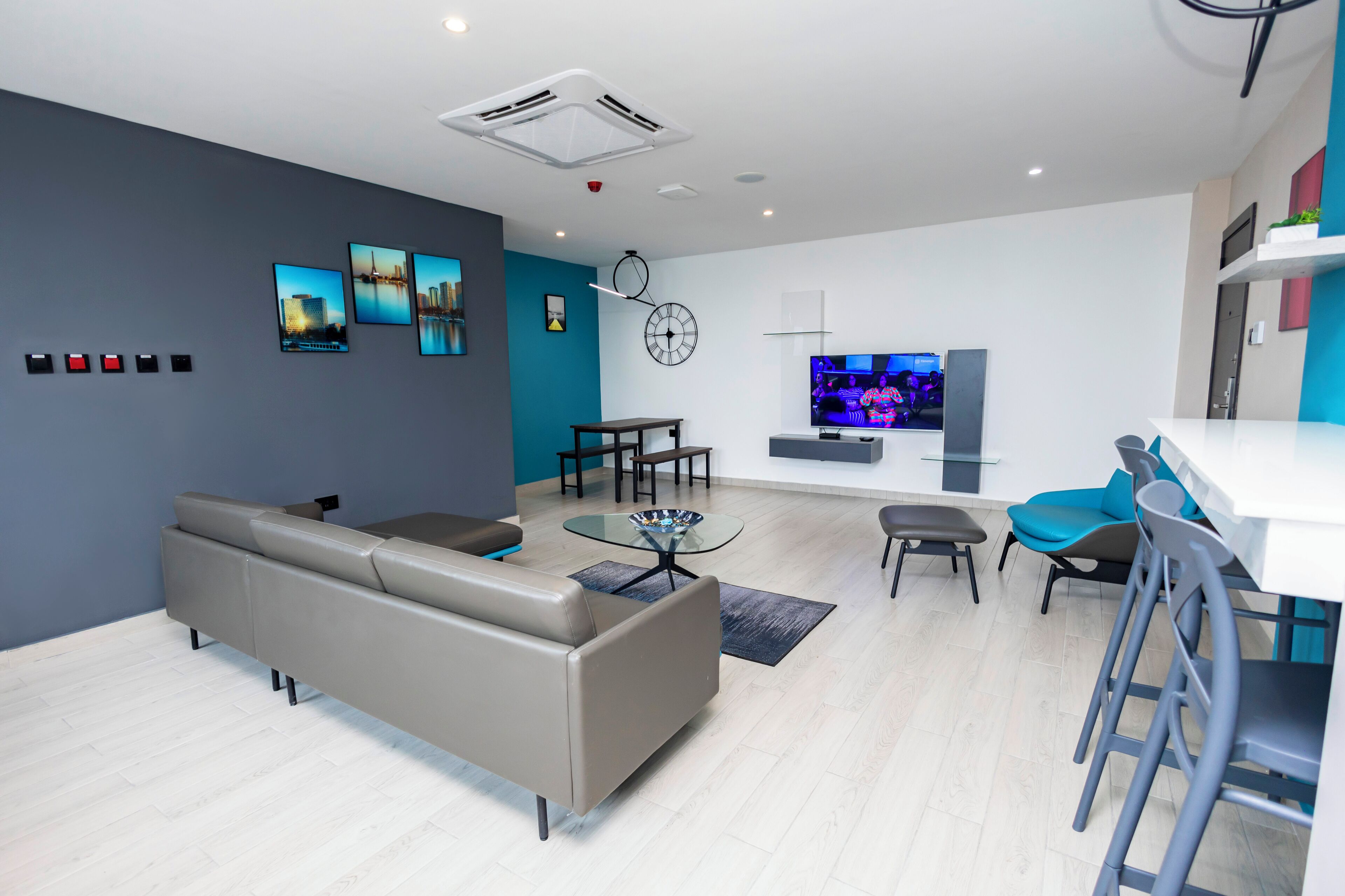 A modern living room with a sofa, a glass coffee table, a TV, and a bar area with stools.