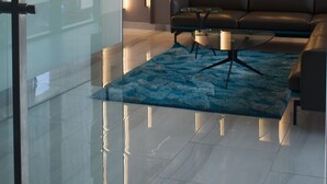 A modern living room with a glass partition, a sofa, a coffee table, and a cityscape view. - Bankable Roomzzz (Accra)