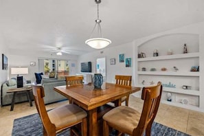 Un coin repas avec une table et des chaises en bois, un ventilateur de plafond et un téléviseur en arrière-plan.