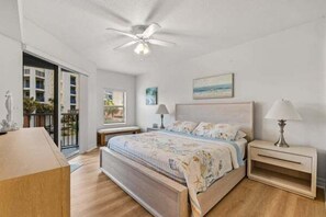 A bedroom with a bed, bedside tables, a ceiling fan, and a view of the outdoors.