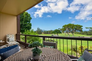 A covered outdoor area with a view of a golf course, featuring a round table with chairs and a potted plant.