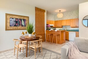 A modern kitchen with wooden cabinets, a dining area with a round table and chairs, and a living area with a sofa.