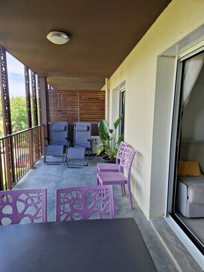 Ein Balkon mit Gartenmöbeln, einem Blumentopf und einer Schiebetür.