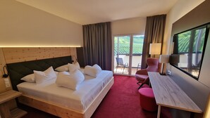 Habitación de hotel con una cama grande, un escritorio, una silla, un televisor y vistas a un paisaje verde por la ventana.