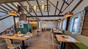 Un restaurante con mesas y sillas de madera, un banco acolchado verde y lámparas colgantes.