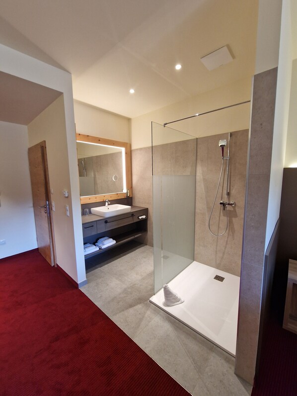 Un baño moderno con ducha envuelta en vidrio, tocador con espejo y suelo cubierto de alfombra roja.
