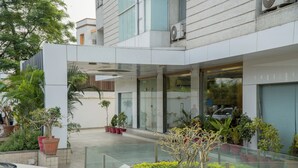 A modern building with a glass entrance, potted plants, and a car parked outside. - The Horizon Hotel (Ankleshwar)