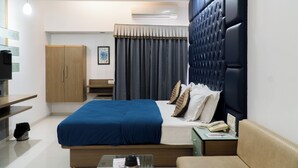A modern hotel room with a large bed, a desk, a wardrobe, and a seating area. - The Horizon Hotel (Ankleshwar)