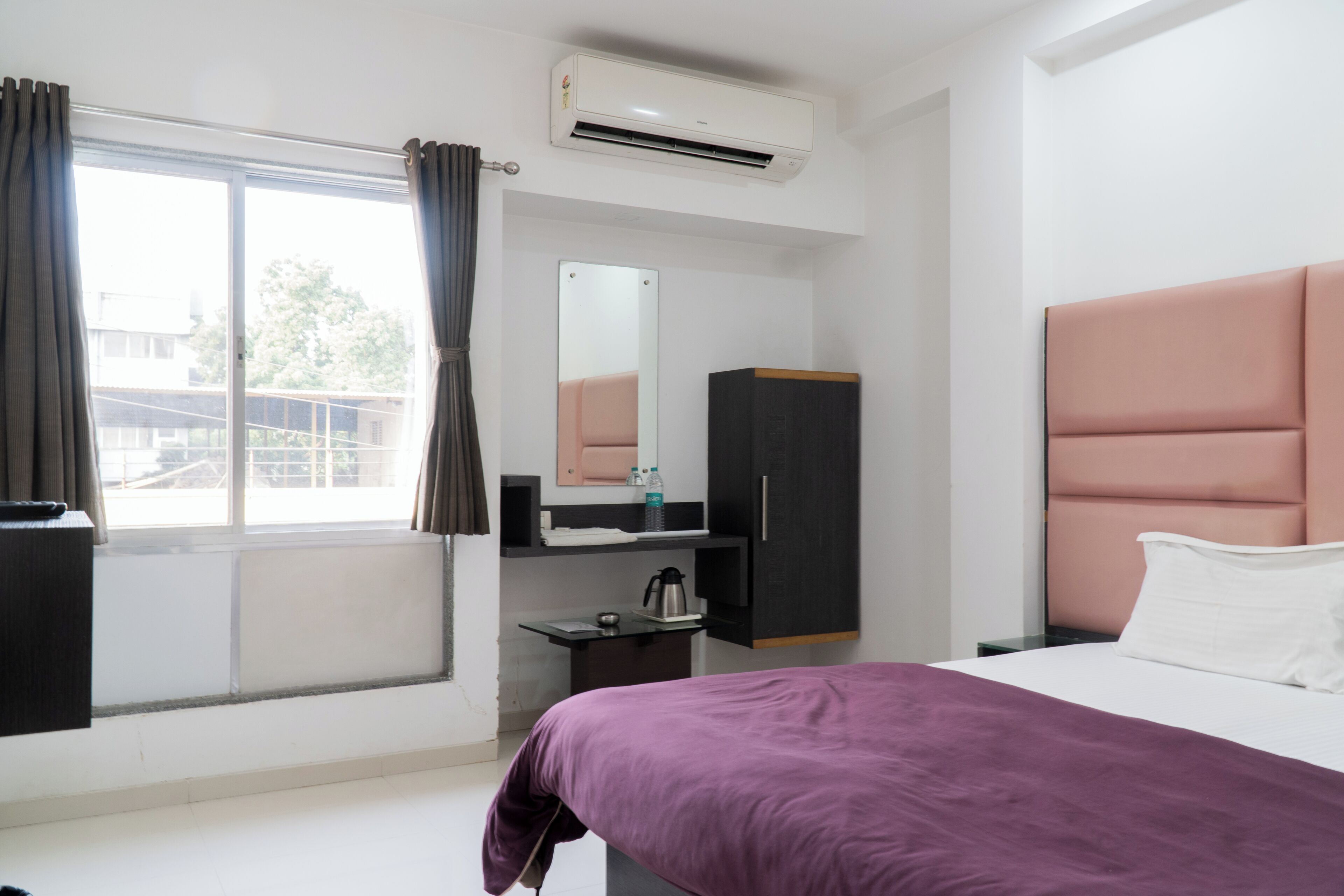 Ein Hotelzimmer mit Bett, Kleiderschrank, Schreibtisch mit Wasserkocher, Spiegel und Klimaanlage.