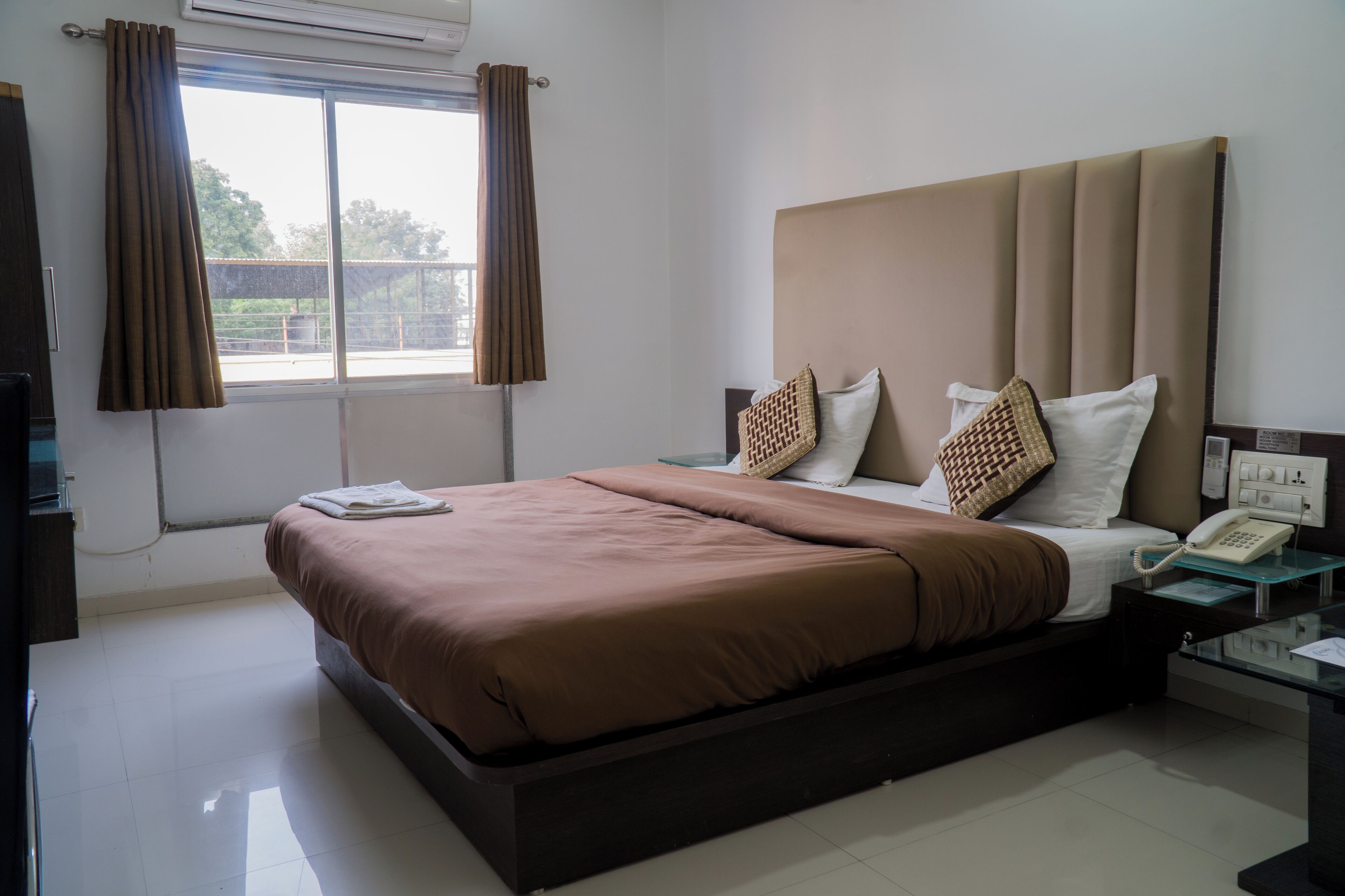 A hotel room with a large bed, a bedside table with a telephone, and a window with curtains.