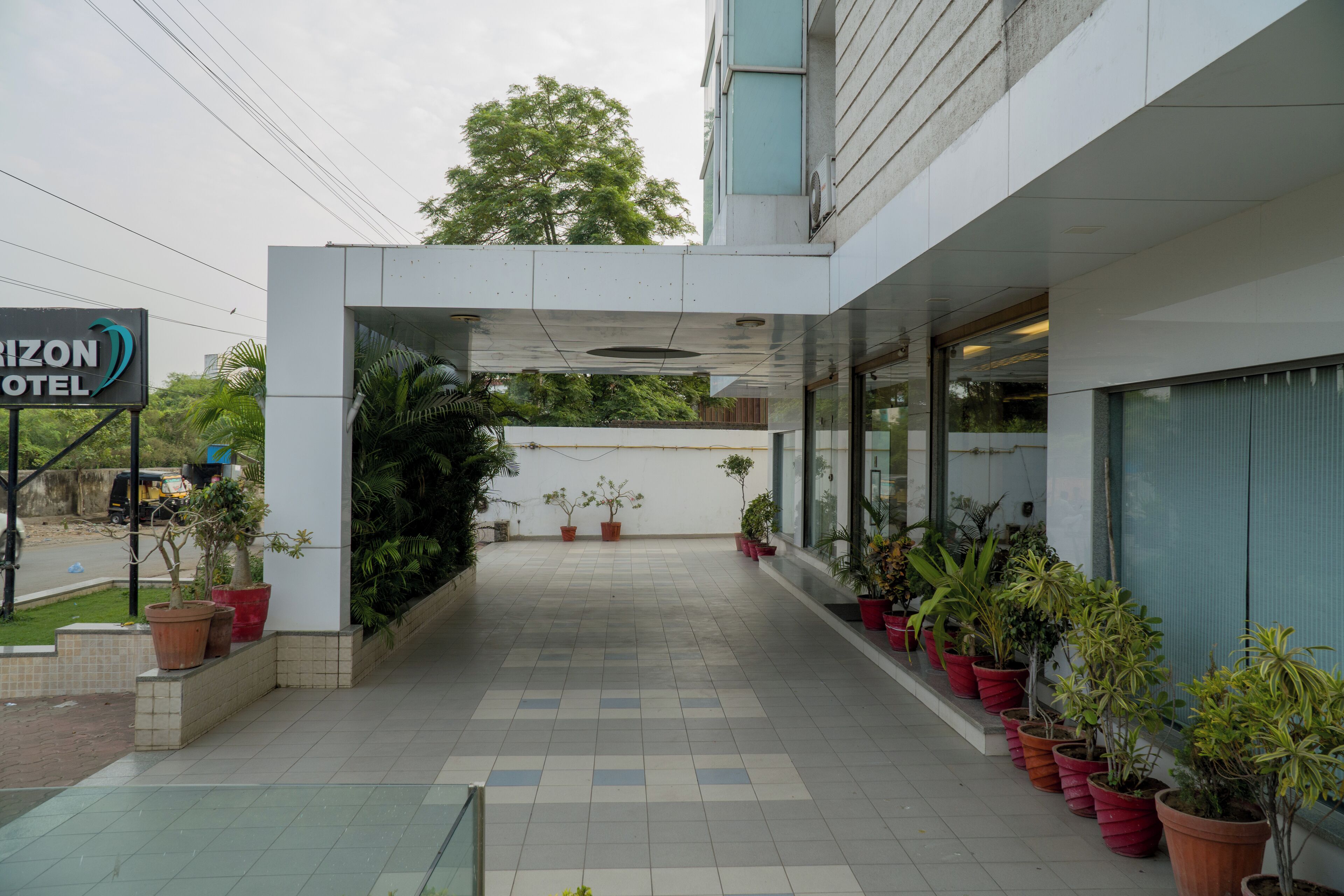 Entrada de un hotel con un letrero que dice "HORIZON HOTEL", un camino de baldosas y plantas en macetas a lo largo del sendero.