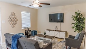 A living room with a ceiling fan, a flat-screen TV, a coffee table, two sofas, a side table, and a potted plant. - Gulf - Charming 2Br Lake Front Apartment (Gulfport)