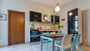 Une cuisine moderne avec des meubles noirs, des appareils en acier inoxydable et un coin repas comprenant une table en verre et des chaises bleues.