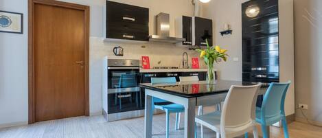 A modern kitchen with black cabinets, stainless steel appliances, and a dining area with a glass table and blue chairs.