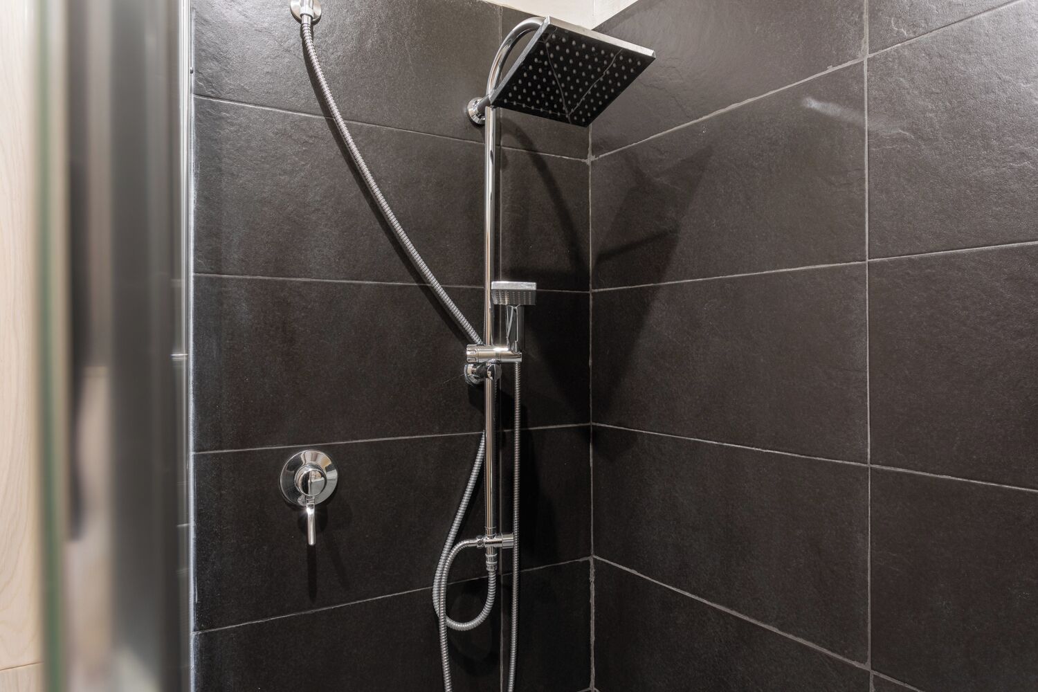 Een douche met een handdouche en een wandmengkraan in een betegelde badkamer.