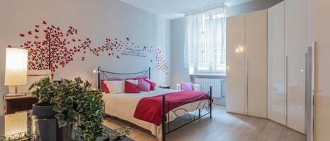 Une chambre à coucher moderne avec un lit, une table de chevet, une lampe et une grande fenêtre.