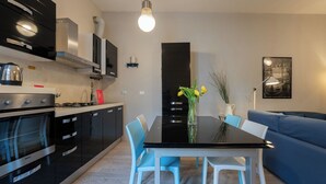 Une cuisine moderne avec un plan de travail noir, des appareils en acier inoxydable et un coin repas comprenant une table noire et des chaises bleues.
