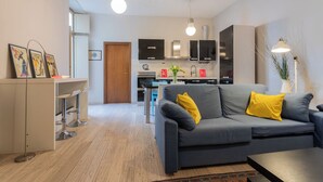 Un salon moderne avec un canapé gris, des coussins jaunes, une table basse et un coin repas comprenant une table et des chaises.