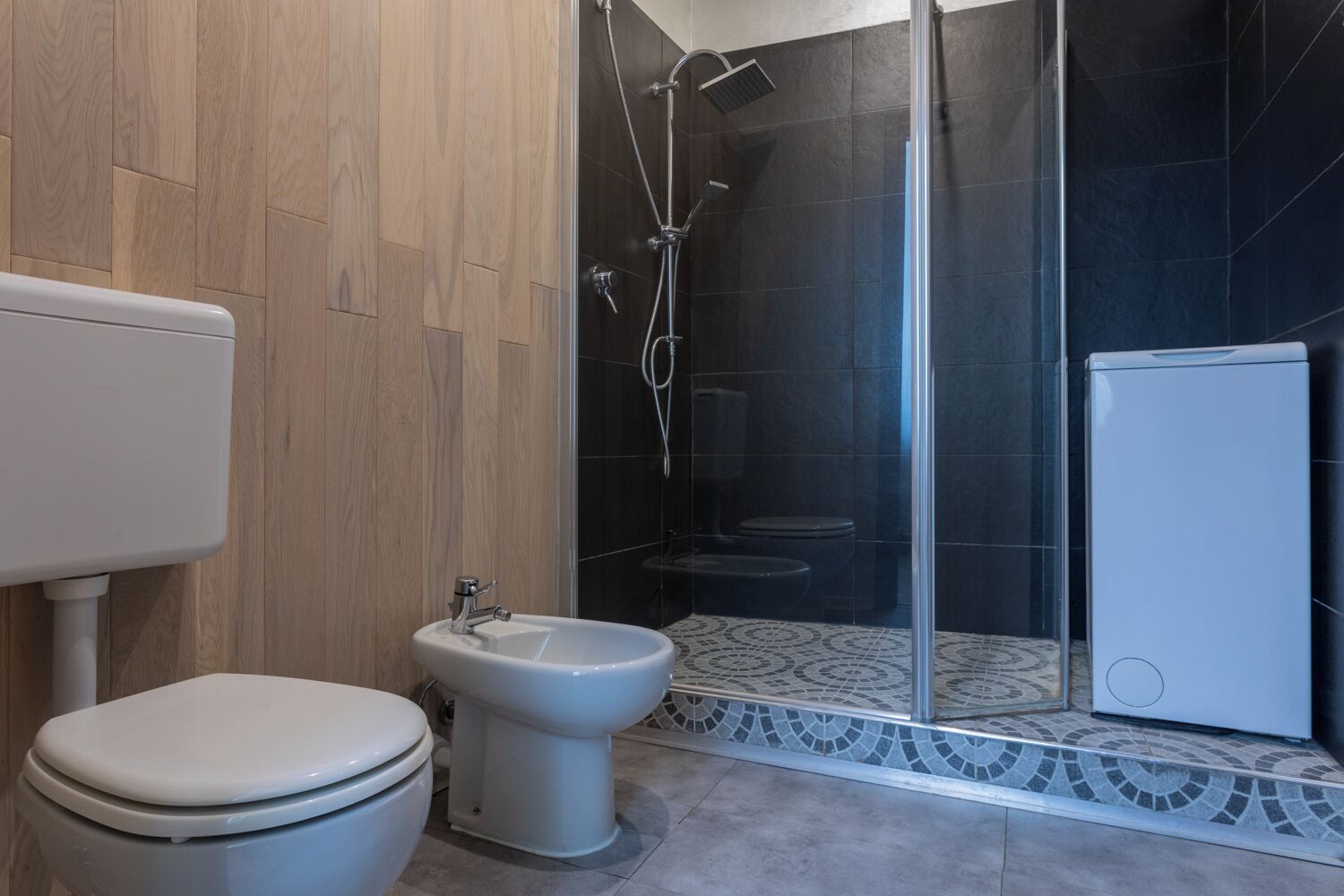 A bathroom with a toilet, bidet, and a glass-enclosed shower area.