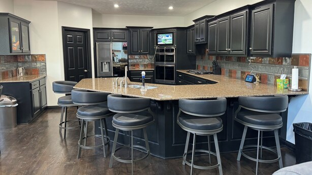 Une cuisine moderne avec des meubles de rangement aux couleurs sombres, un plan de travail en granit et un îlot central intégré avec des tabourets de bar.