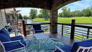 Une terrasse couverte avec des sièges d’extérieur, une vue sur un terrain de golf et un plan d’eau.