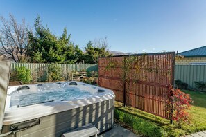 Un bain à remous dans un jardin, avec une clôture en bois, un petit potager et une montagne en arrière-plan.