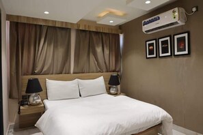 Ein Hotelzimmer mit einem großen Bett, zwei Nachttischen mit Lampen, einer Deckenklimaanlage und drei gerahmten Bildern an der Wand.