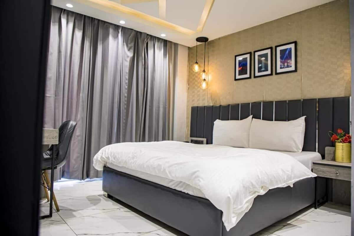 A modern hotel room with a large bed, a desk, and a chair.