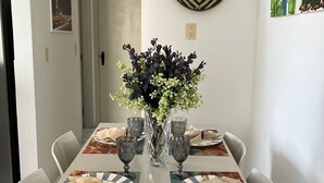 A dining area with a white table set for four, featuring a vase with flowers, four glasses, and plates with napkins. - Beautiful and cozy flat. Complete and just 50 m from the beach  (Candeias Jaboatão dos Guararapes)