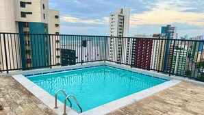 A rectangular pool with a metal ladder on a tiled deck, surrounded by a black metal fence, with high-rise buildings in the background. - Beautiful and cozy flat. Complete and just 50 m from the beach  (Candeias Jaboatão dos Guararapes)