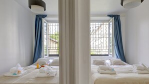Habitación de hotel con dos camas, un ventanal con barrotes y vistas a edificios.