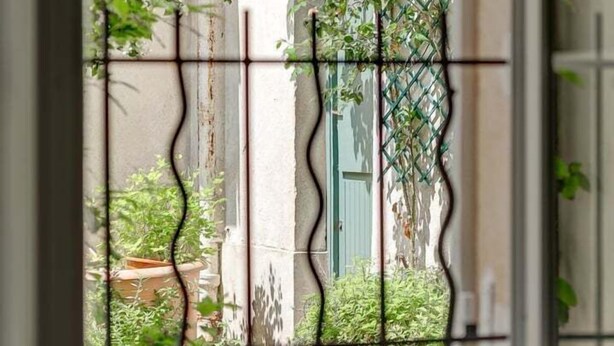Vista a través de una ventana con una reja metálica, una mesa con platos verdes y una silla.