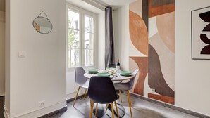 Comedor con una mesa dispuesta para cuatro personas, una ventana con cortinas y un cuadro abstracto geométrico en la pared.