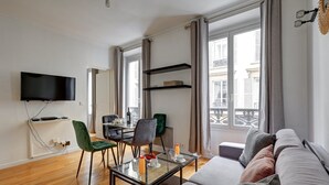 A modern living room with a flat-screen TV, a glass coffee table, a sofa, and a dining area with chairs and a table. - 316 Suite BIOT 5 - Superb apartment in Paris (Paris 17 Batignolles-Monceau)