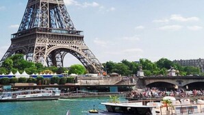A Torre Eiffel com um rio e barcos ao primeiro plano.