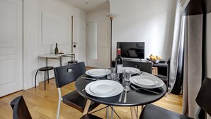 A dining area with a round table set for four, a television, and a small kitchen area with a refrigerator and a microwave. - 395 Suite BIOT 10 - Superb apartment in Paris (Paris 17 Batignolles-Monceau)