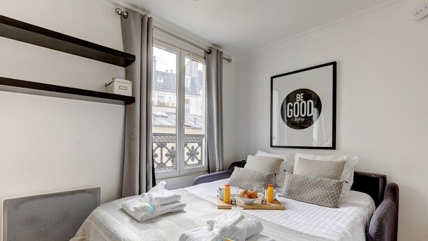 A neatly made bed with a breakfast tray, a framed motivational quote, and a view of buildings through the window. - 395 Suite BIOT 10 - Superb apartment in Paris (Paris 17 Batignolles-Monceau)