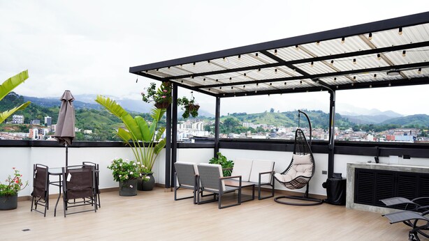 Eine Dachterrasse mit überdachter Sitzgruppe, Topfpflanzen und Blick auf eine Stadtlandschaft und Berge.