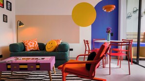 Ein modernes Wohnzimmer mit einem grünen Sofa, orangefarbenen und gelben runden Wanddekorationen, einem violetten Couchtisch und roten Sesseln.