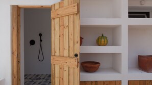 A wooden door leading to a bathroom with a shower, a tiled floor, and shelves with a bowl and a pumpkin. - FLH Jacaranda Costa Caparica Beach House (Almada)