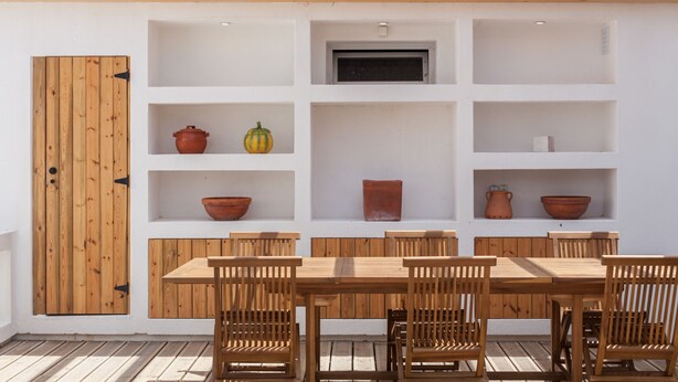 A wooden dining table with six chairs, surrounded by white shelves with various items. - FLH Jacaranda Costa Caparica Beach House (Almada)