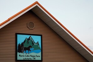 A building with a framed sign that reads "Norris Lake Haven Farm LaFollette, TN" featuring a mountain, trees, and a horse.