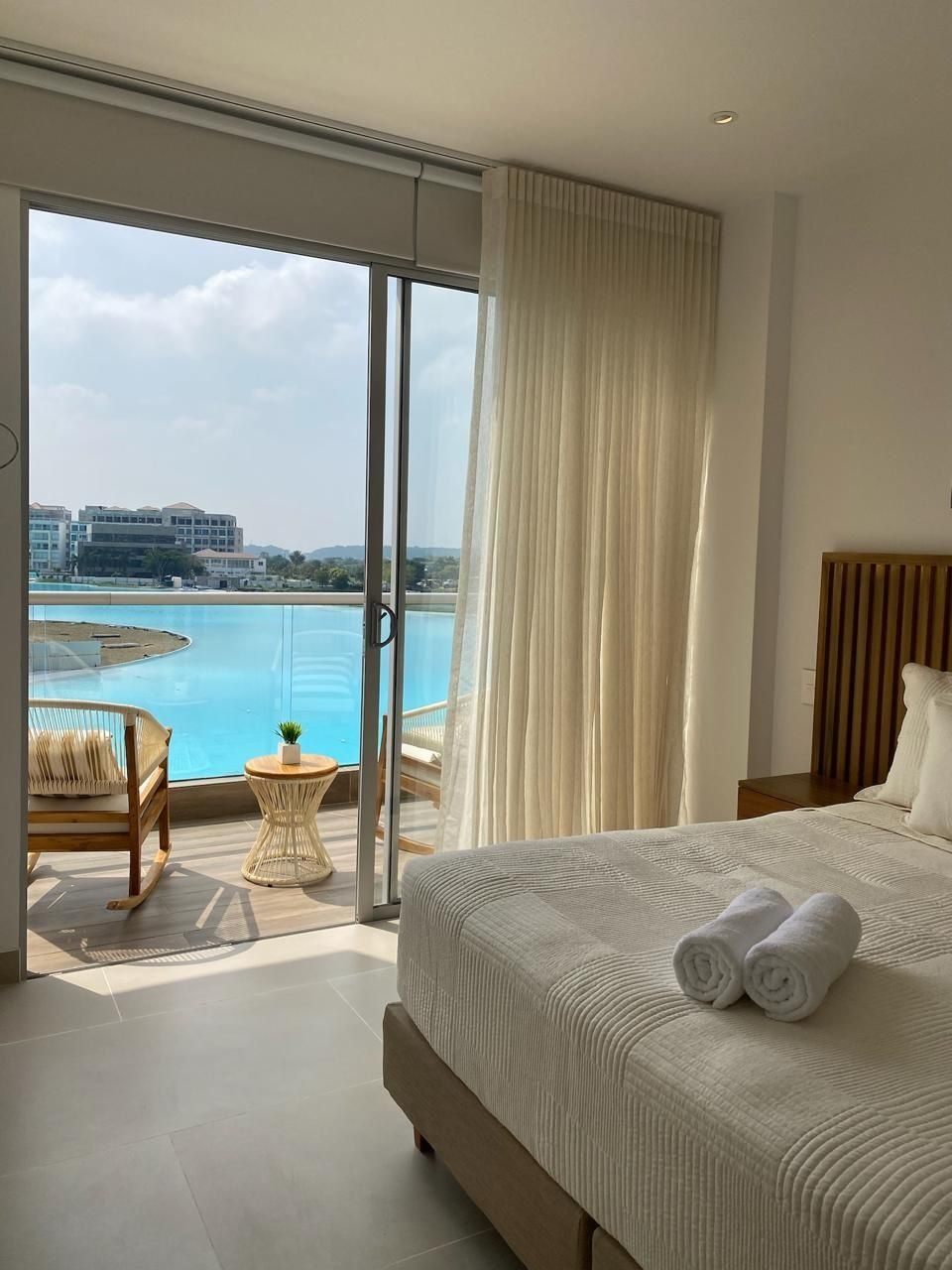 A hotel room with a large bed, a view of a pool, and a chair by the window.